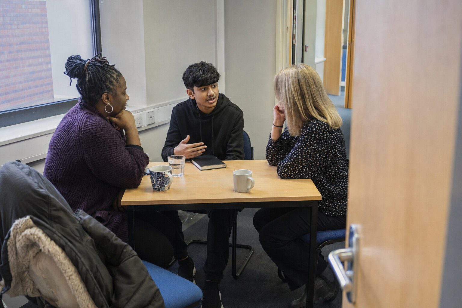 A foster carer and a teacher sitting across a table in a school meeting room, talking over paperwork