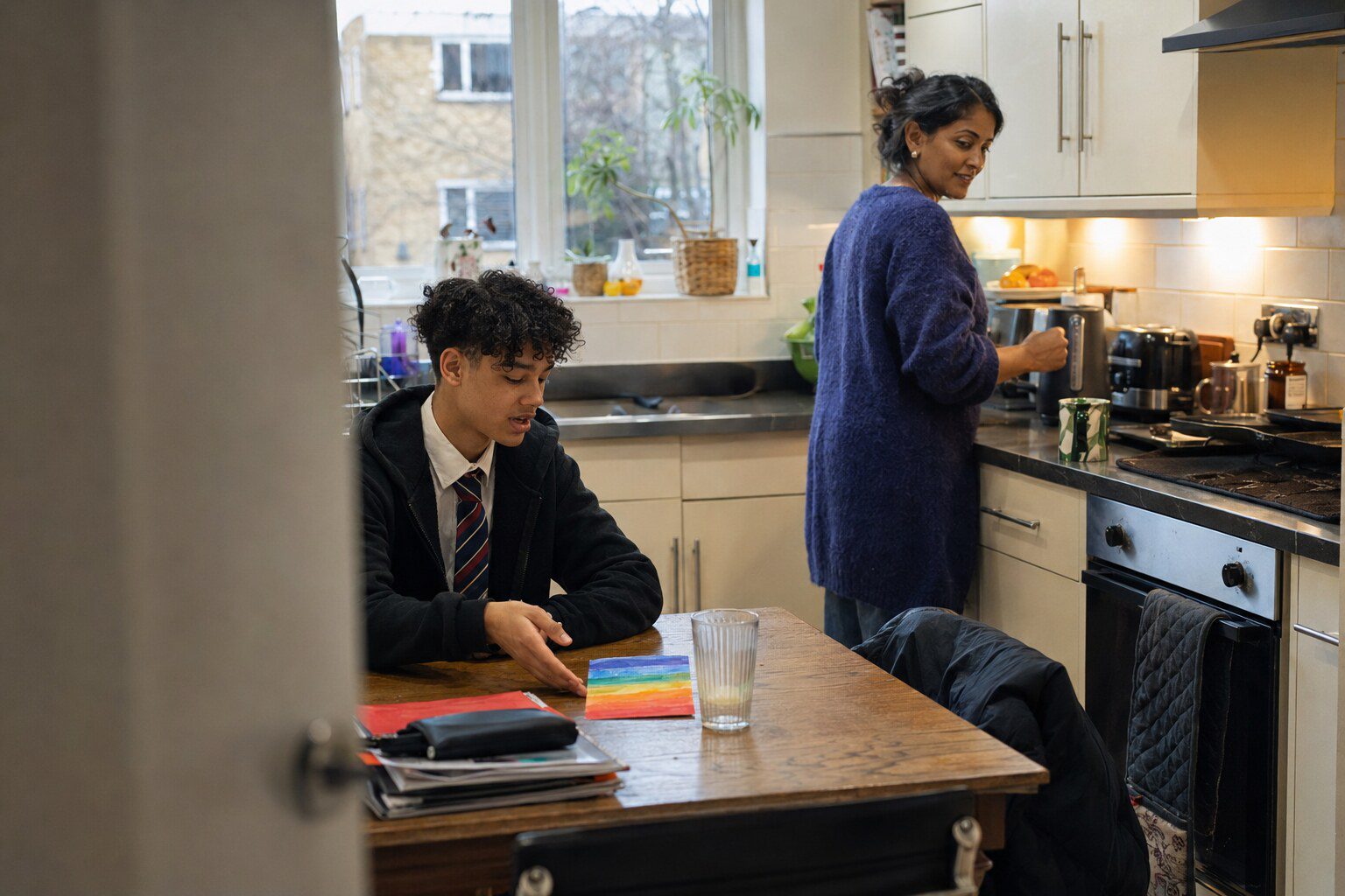 A young person and a foster carer sitting together in a bright living room, relaxed and mid-conversation