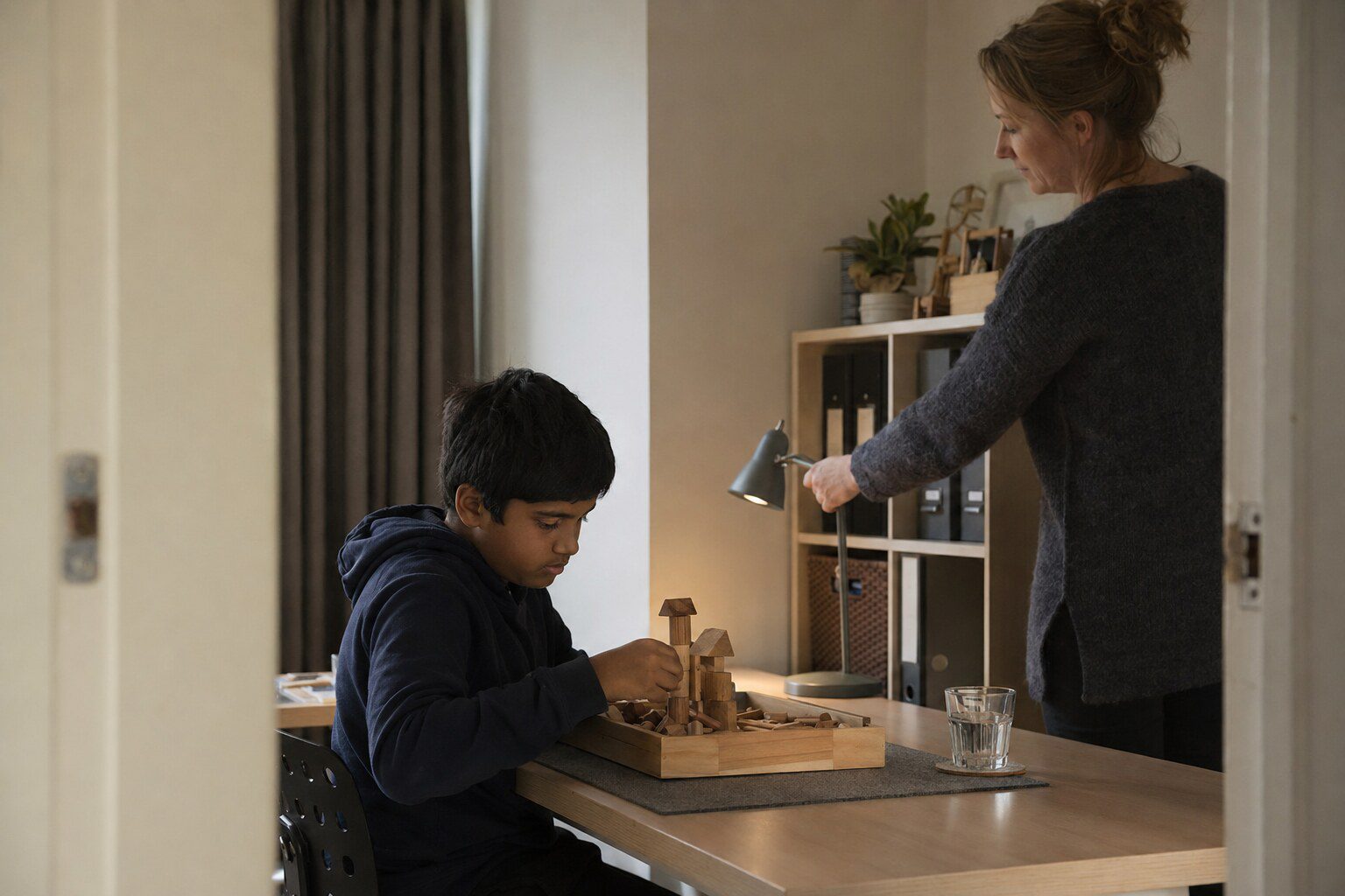 A foster carer sitting on the floor beside a young child, both concentrating on a row of coloured wooden blocks.