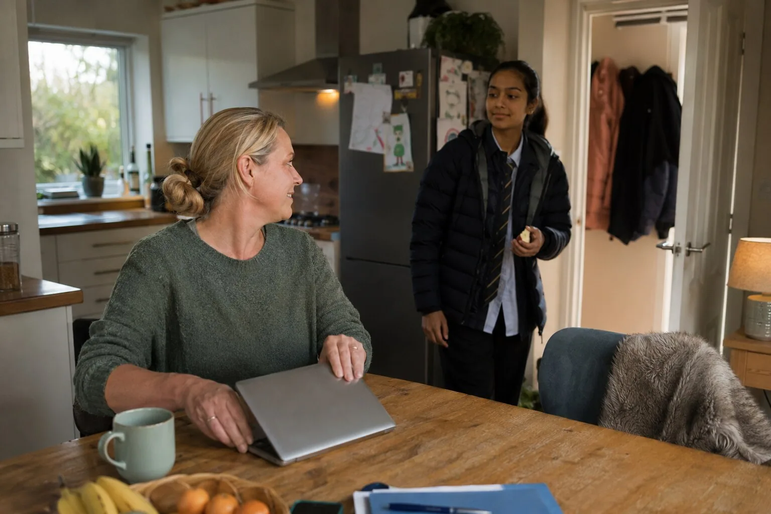 A woman closing her laptop to talk to a teenager arriving home