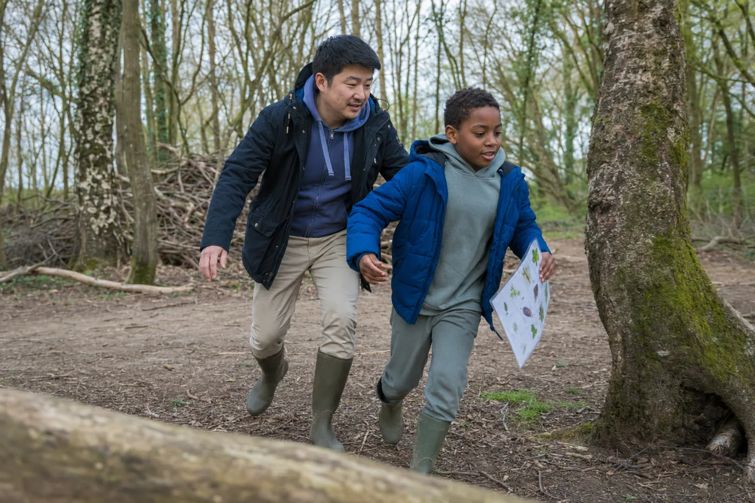 An adult and a child exploring a wooded park with a trail sheet