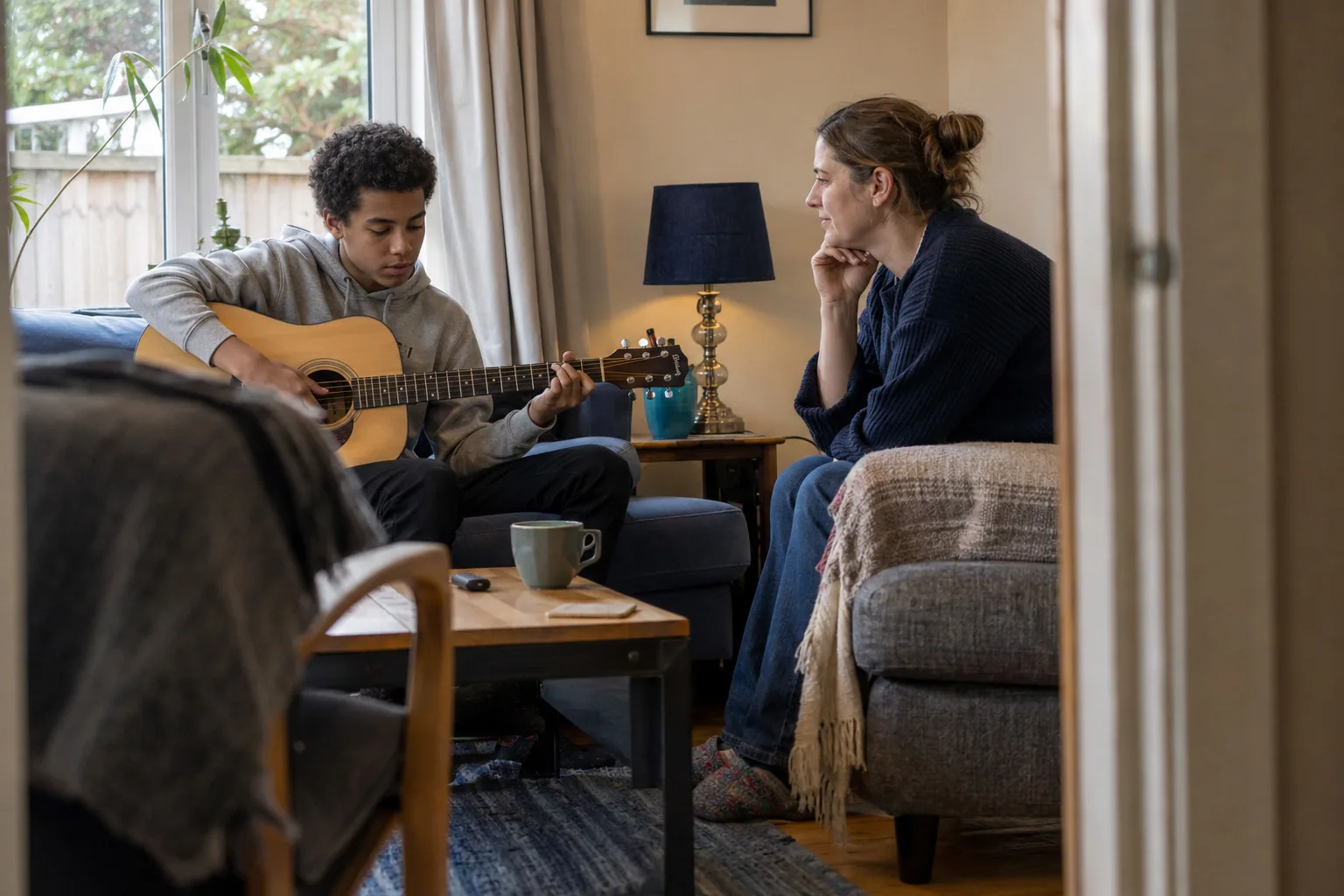 An adult listening while a teenager plays an acoustic guitar