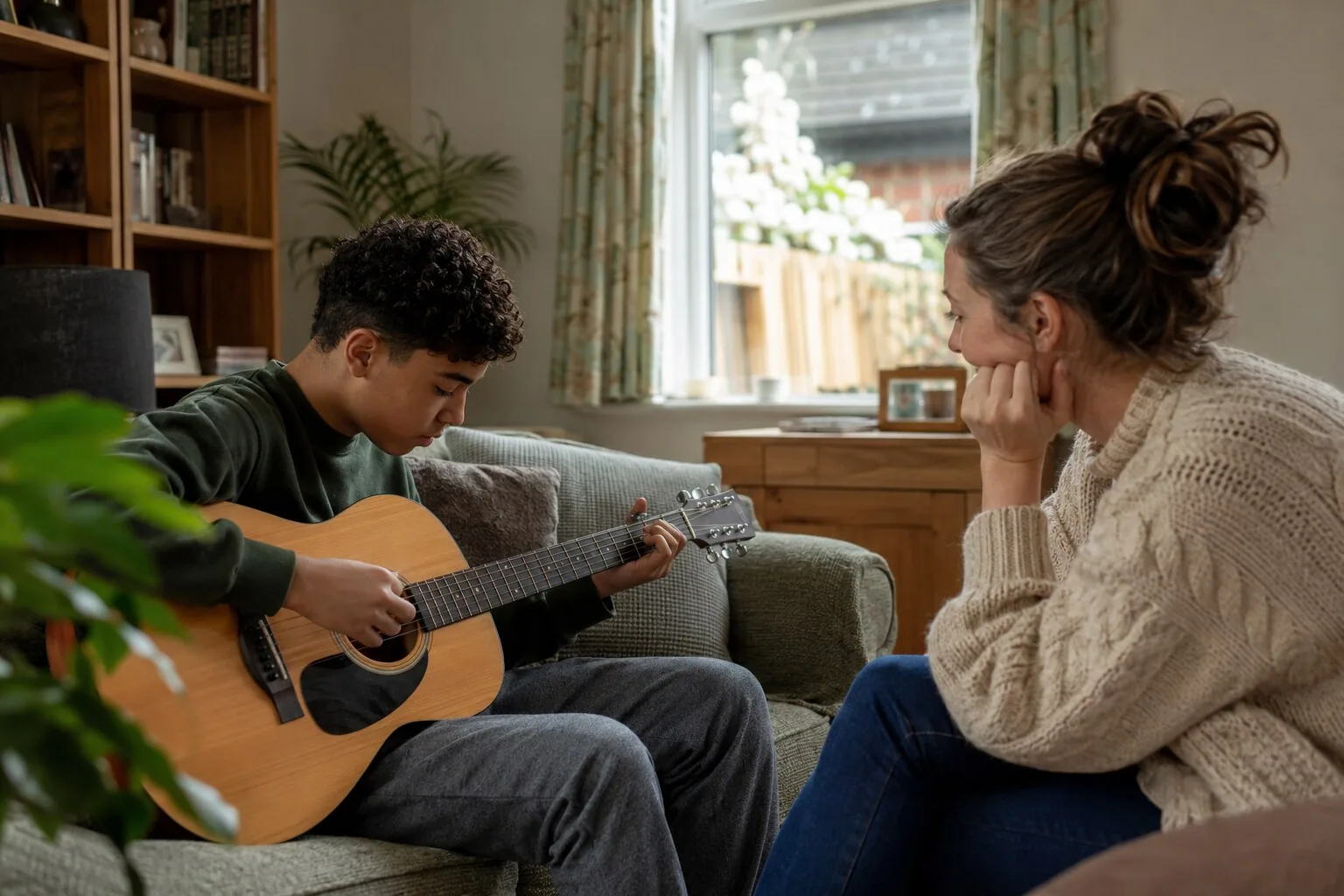 An adult listening to a teenager practising the guitar