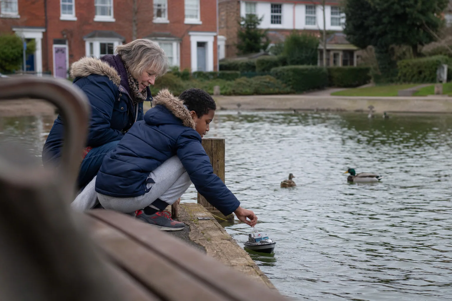 A young person crouching beside a pond with an adult nearby