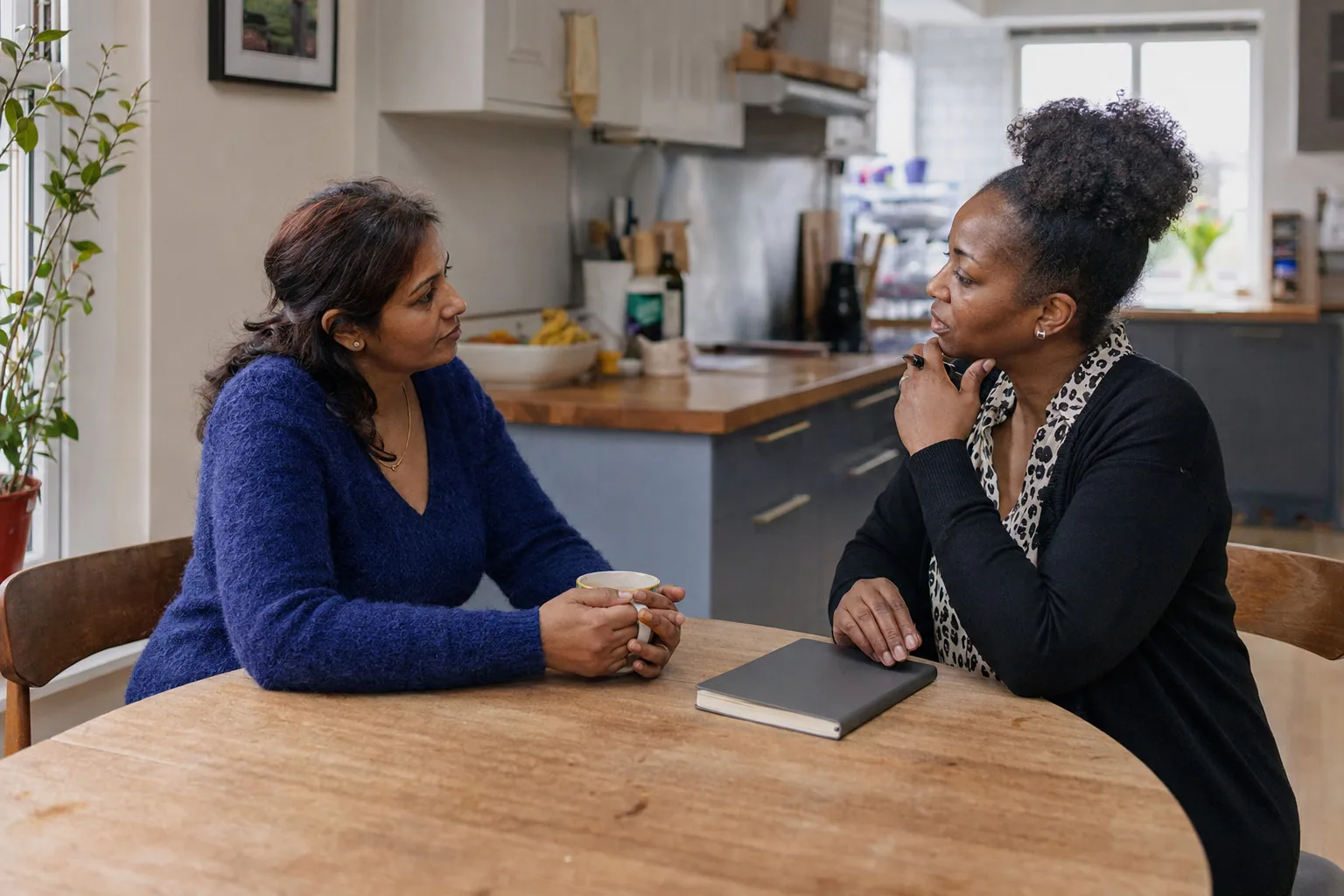 Two adults having a conversation over mugs at the kitchen table