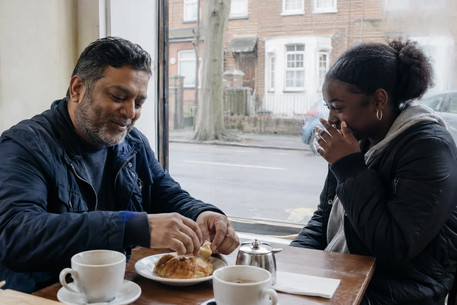 A man and a teenager sharing a laugh at a cafe table