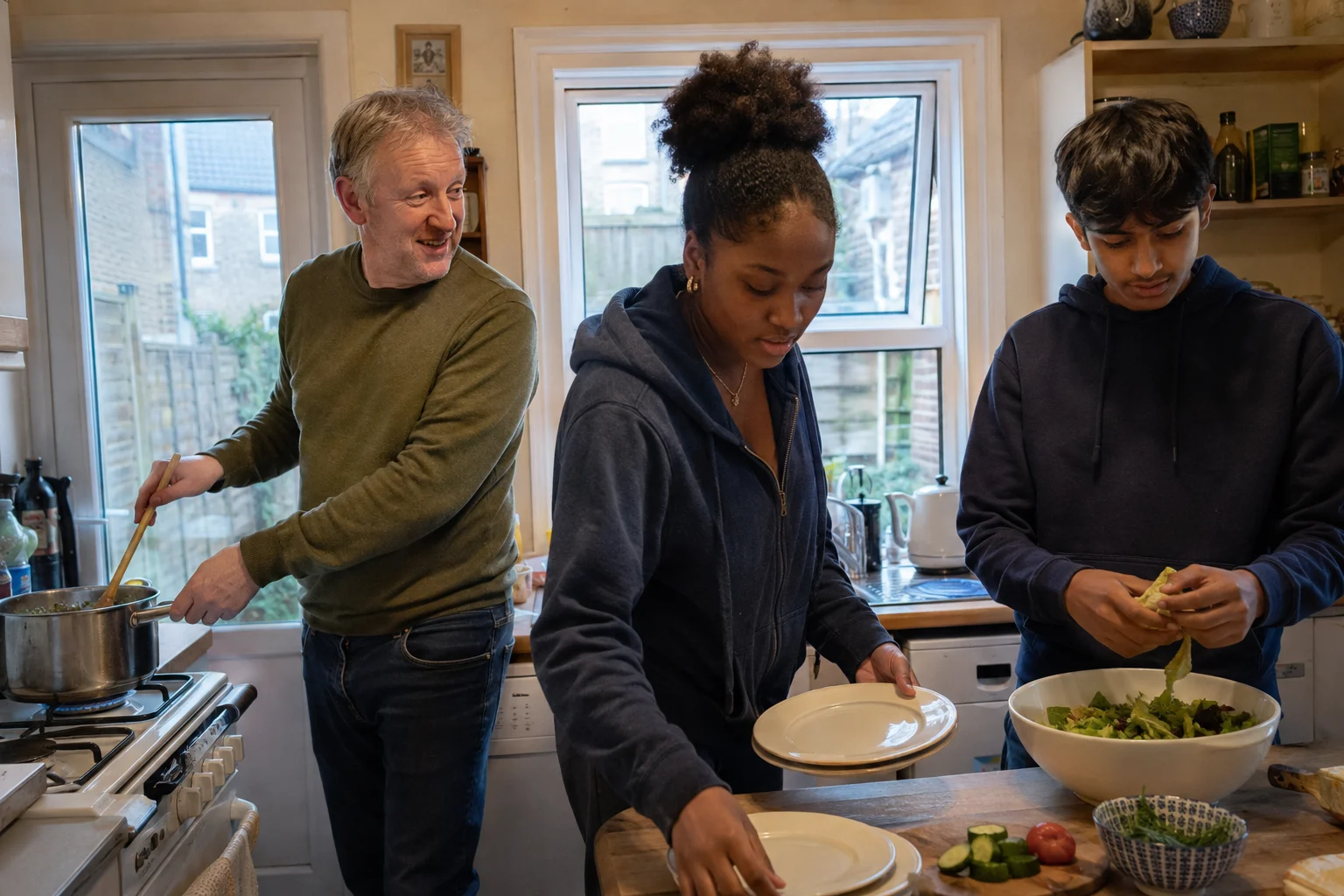 An adult and two teenagers sharing the jobs while preparing dinner