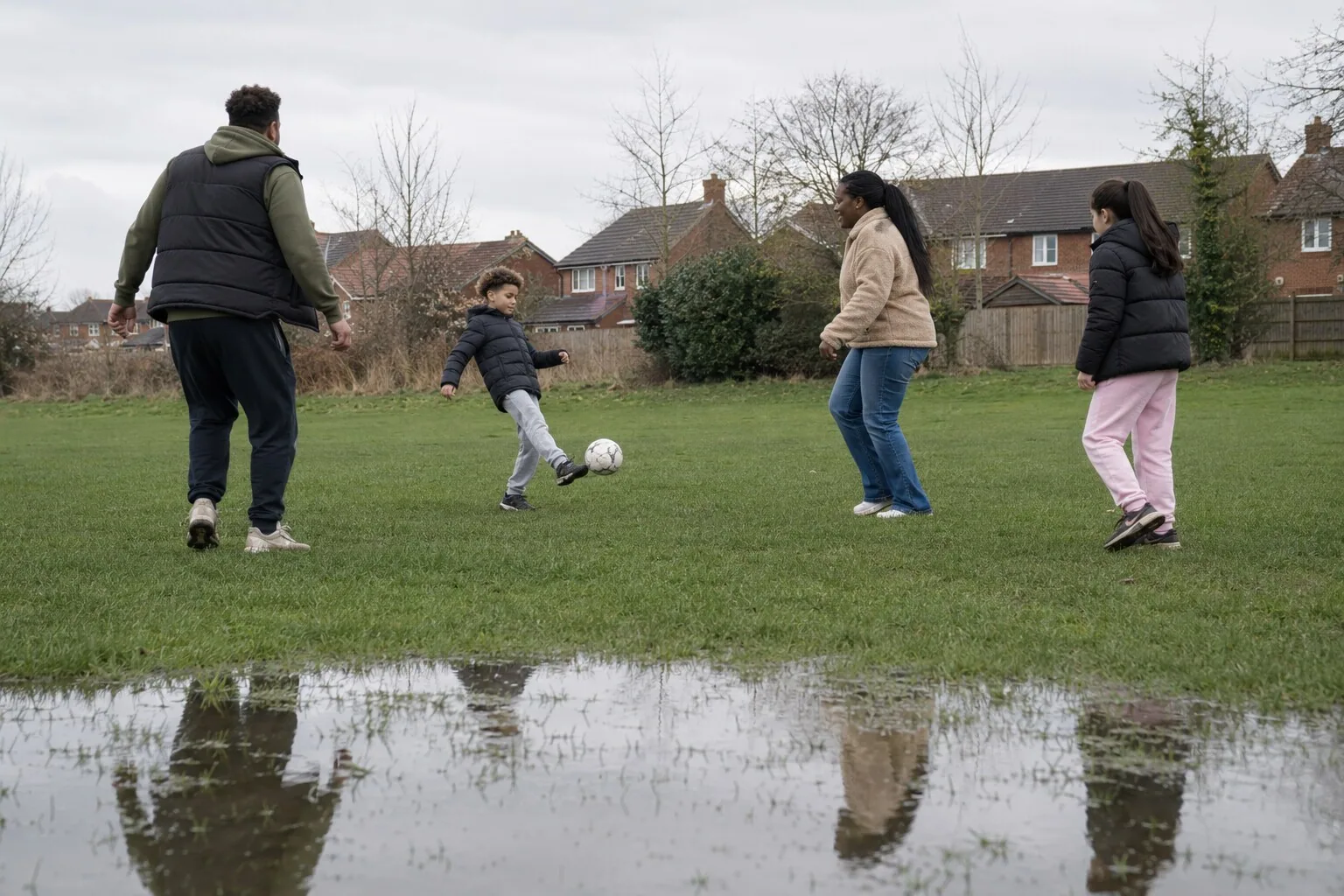 Adults and children playing football together on a neighbourhood field
