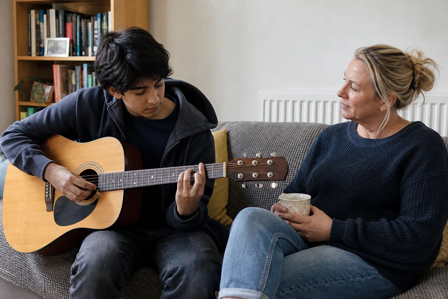 A woman listening while a teenager practises the guitar