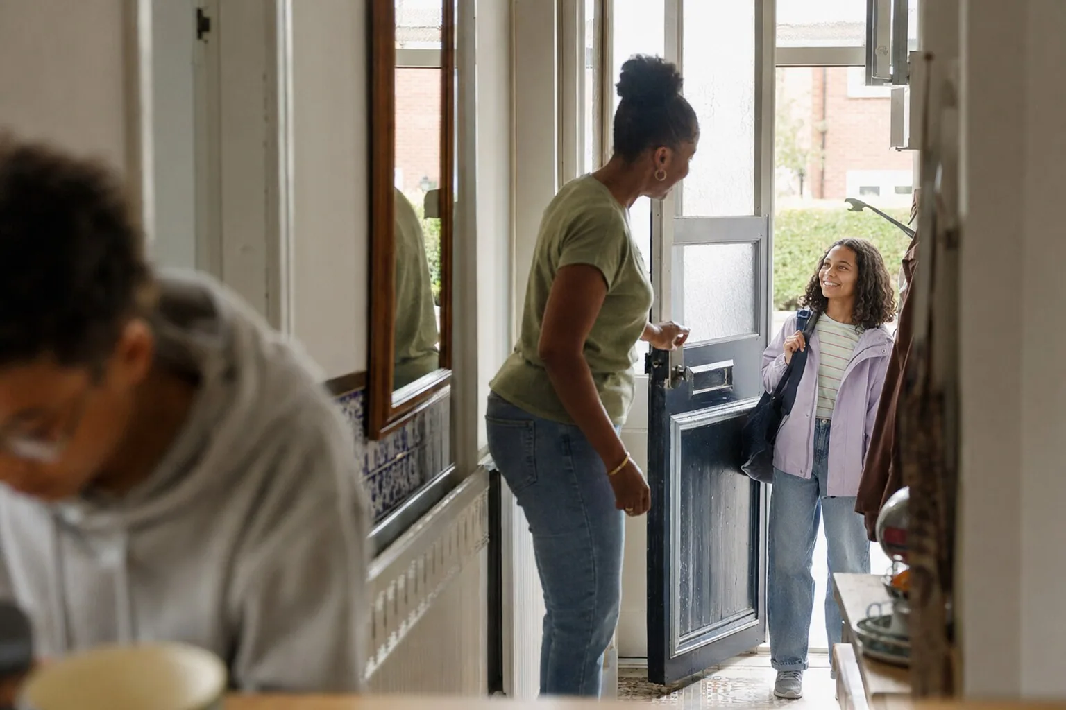 An adult welcoming a young person through the front door