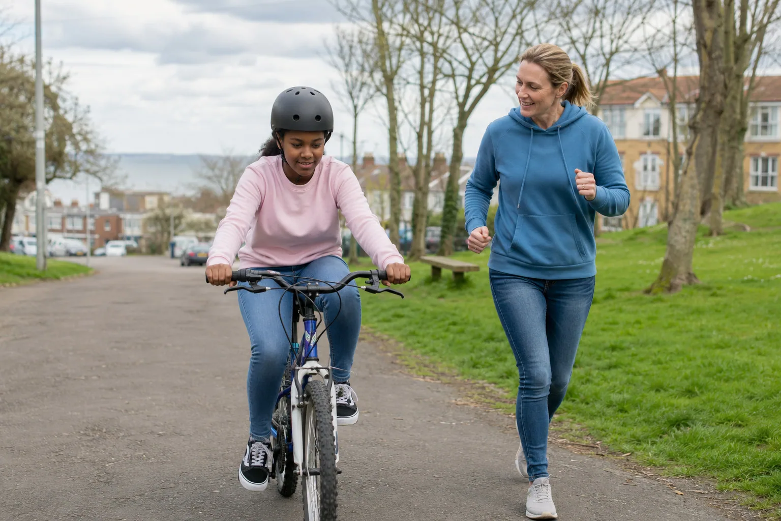 An adult jogging beside a teenager practising on a bicycle in a park