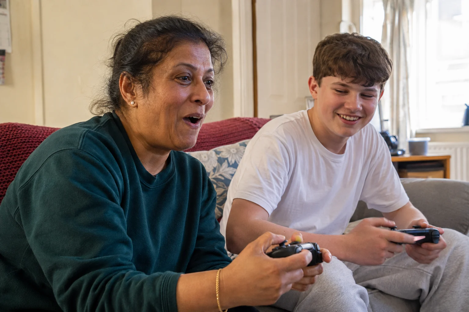 A woman and a teenager laughing while playing a video game