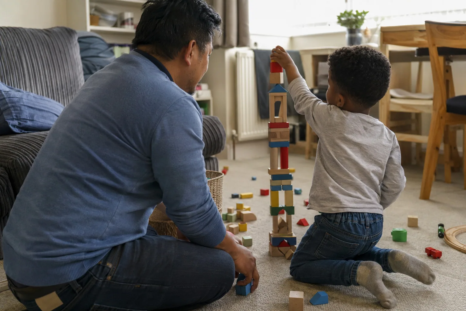 An adult and a young child building a tall tower of blocks on the floor