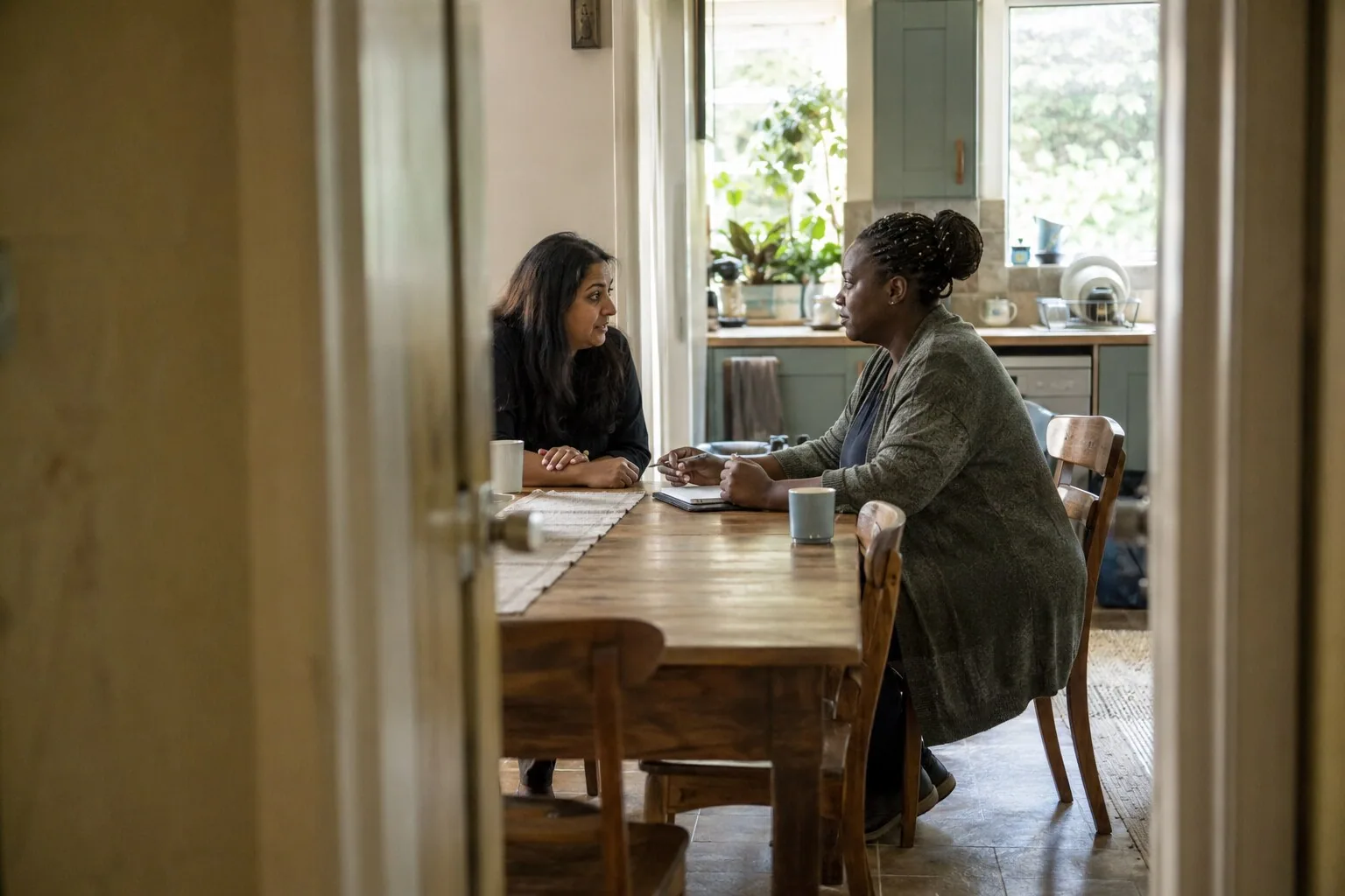 Two adults talking together over mugs at a kitchen table