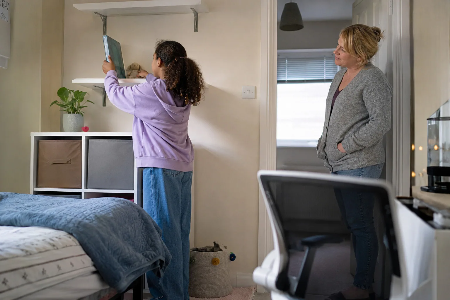 An adult watching a young person pin up pictures in their room