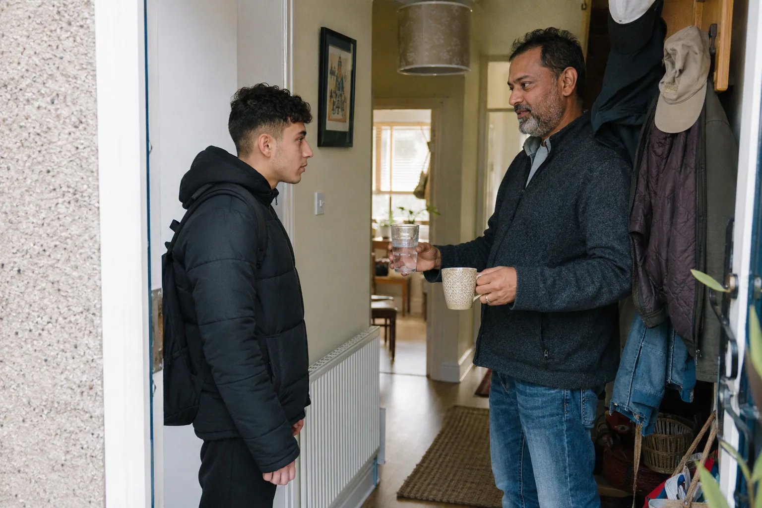 An adult greeting a young person in the hallway with two mugs