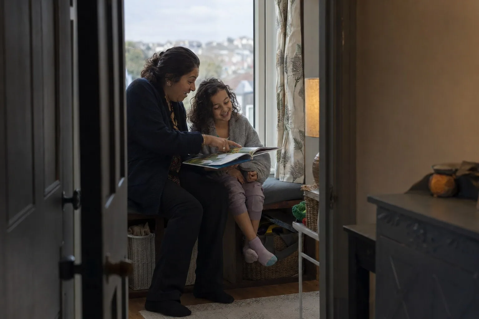 An adult and a child reading together beside a window