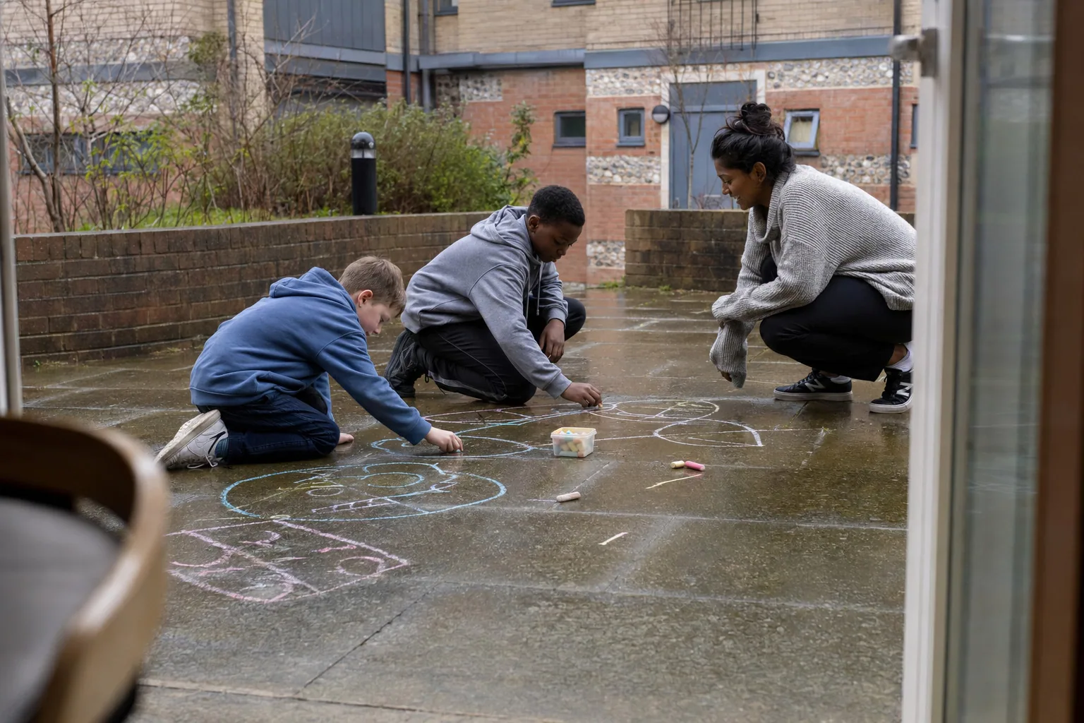 An adult and two children drawing with chalk on a courtyard pavement