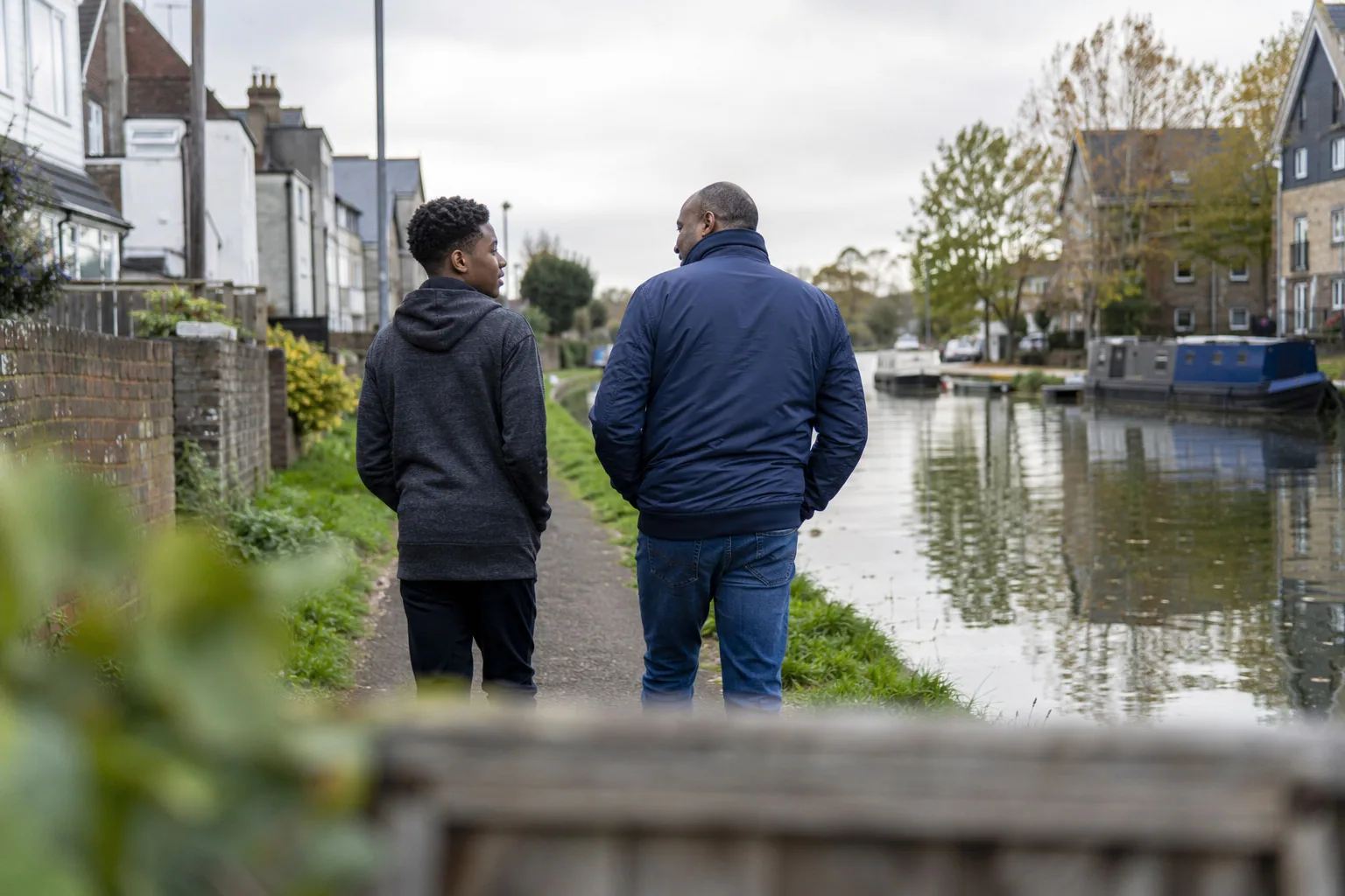 An adult and a teenager walking together beside a residential canal