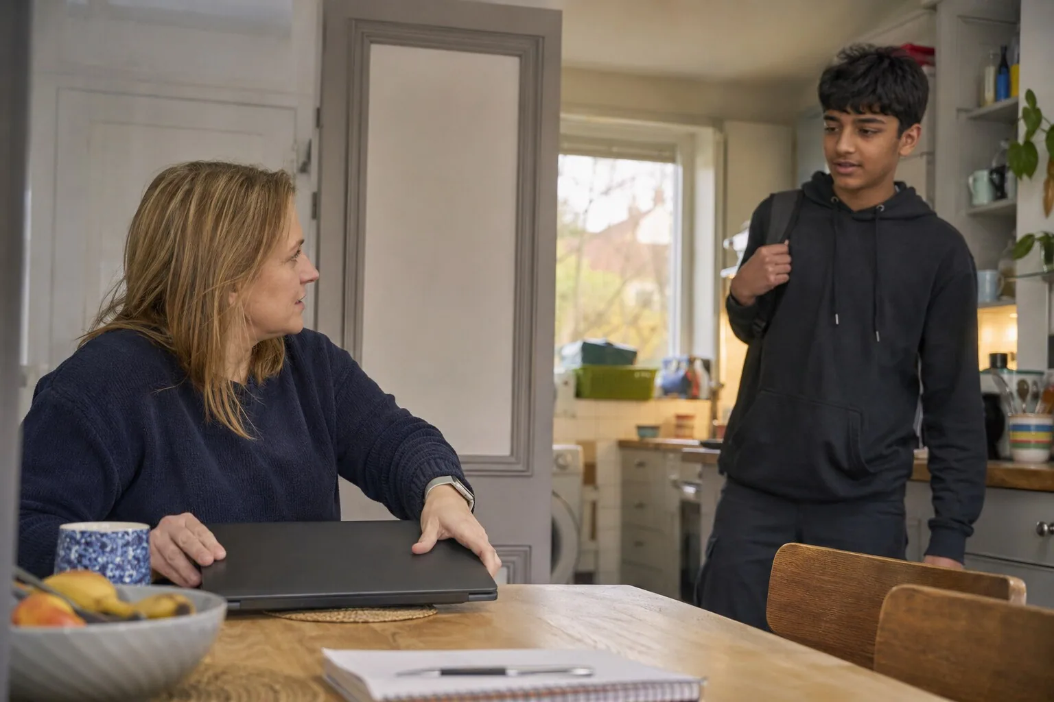 An adult closing a laptop to talk to a teenager arriving home