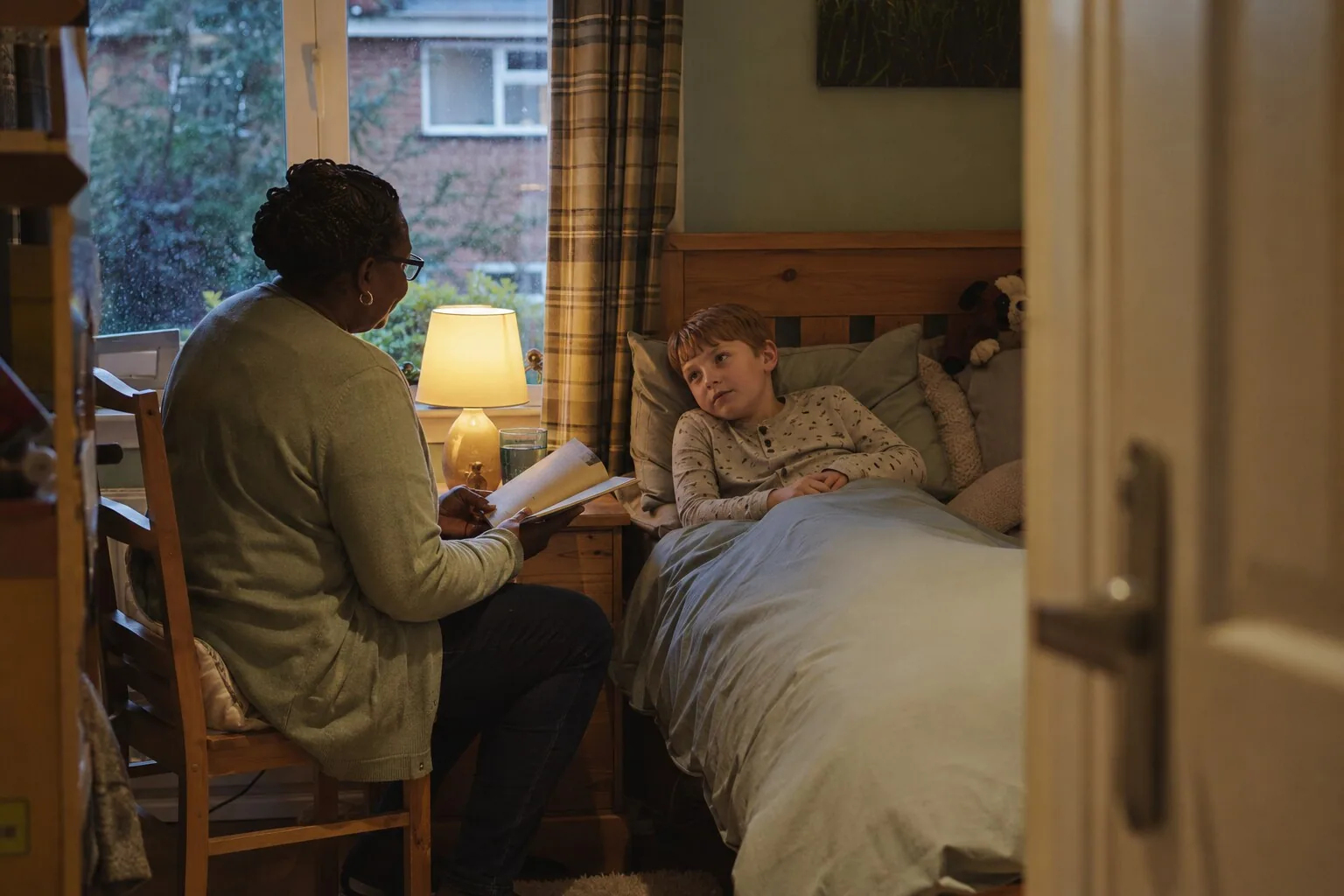 An adult reading beside a child tucked up in bed