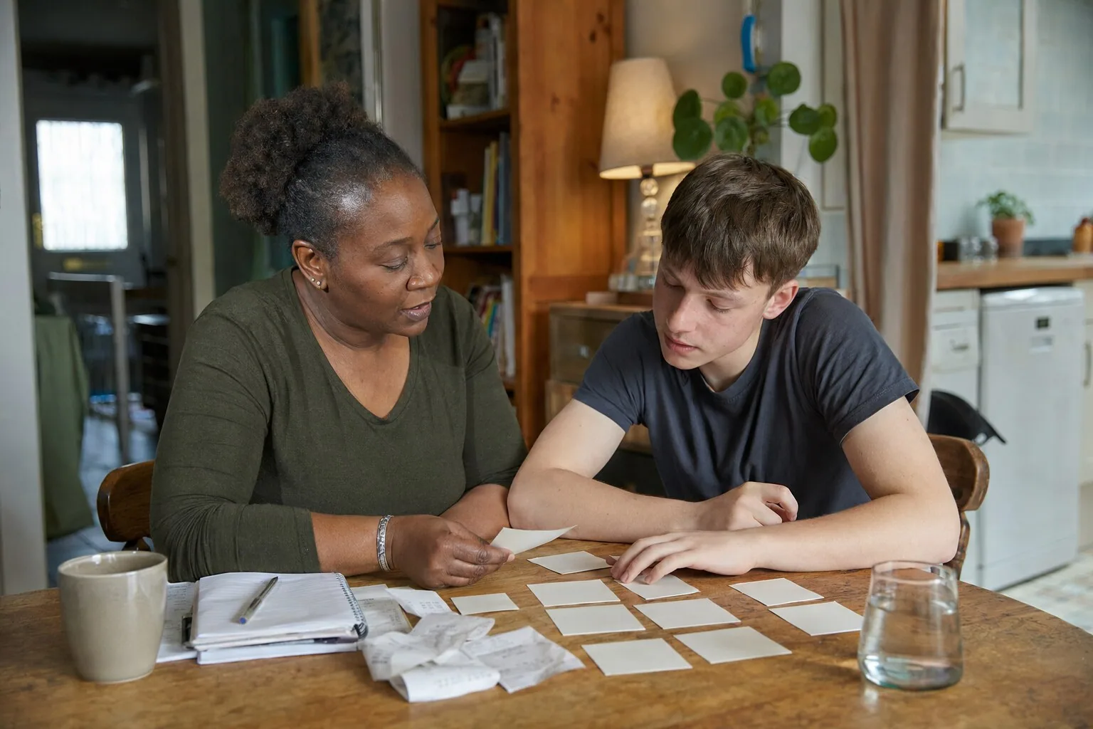 An adult and a teenager arranging small cards together on a table