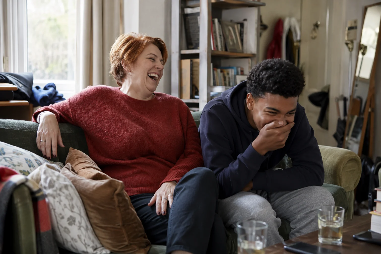 A woman and a teenager laughing together on the sofa
