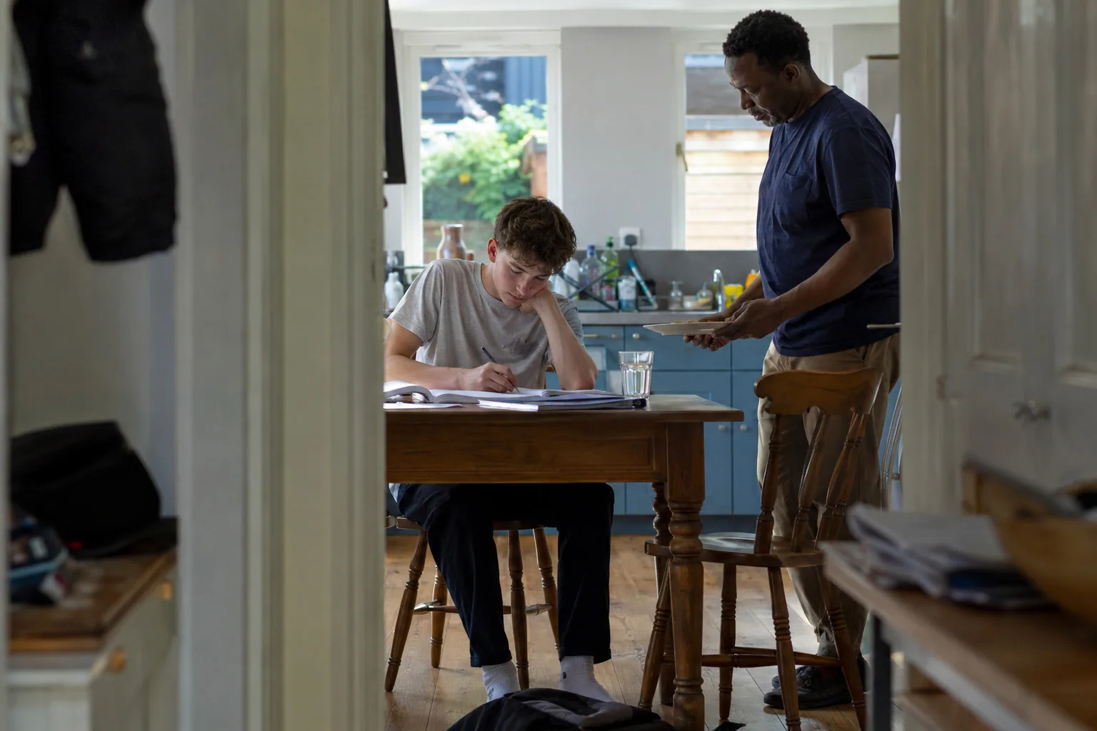 An adult bringing a drink to a teenager studying at the table