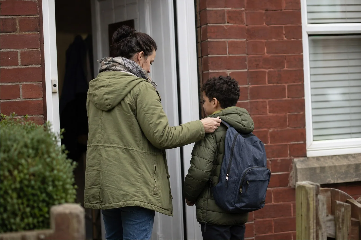 An adult and a child with a backpack setting off from their front door