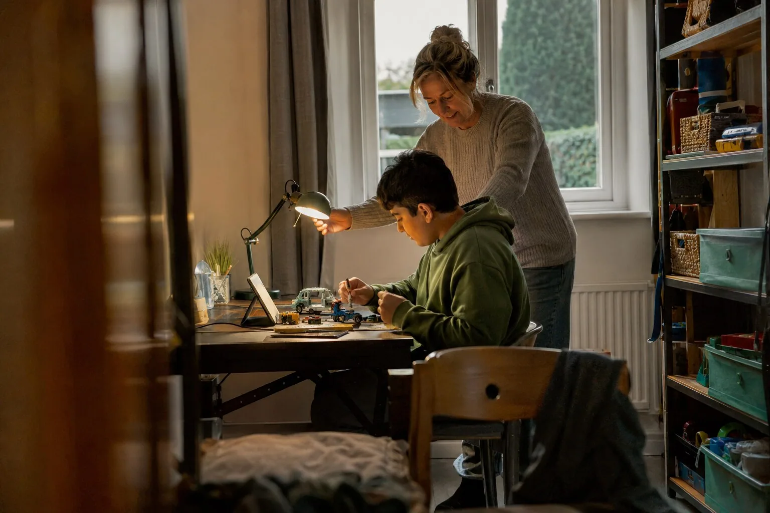 An adult adjusting a desk lamp while a child works on a small project