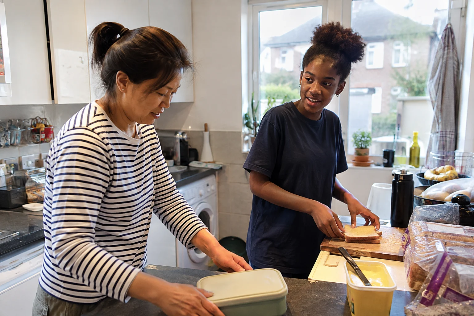 A woman and a teenager making packed lunches in the kitchen