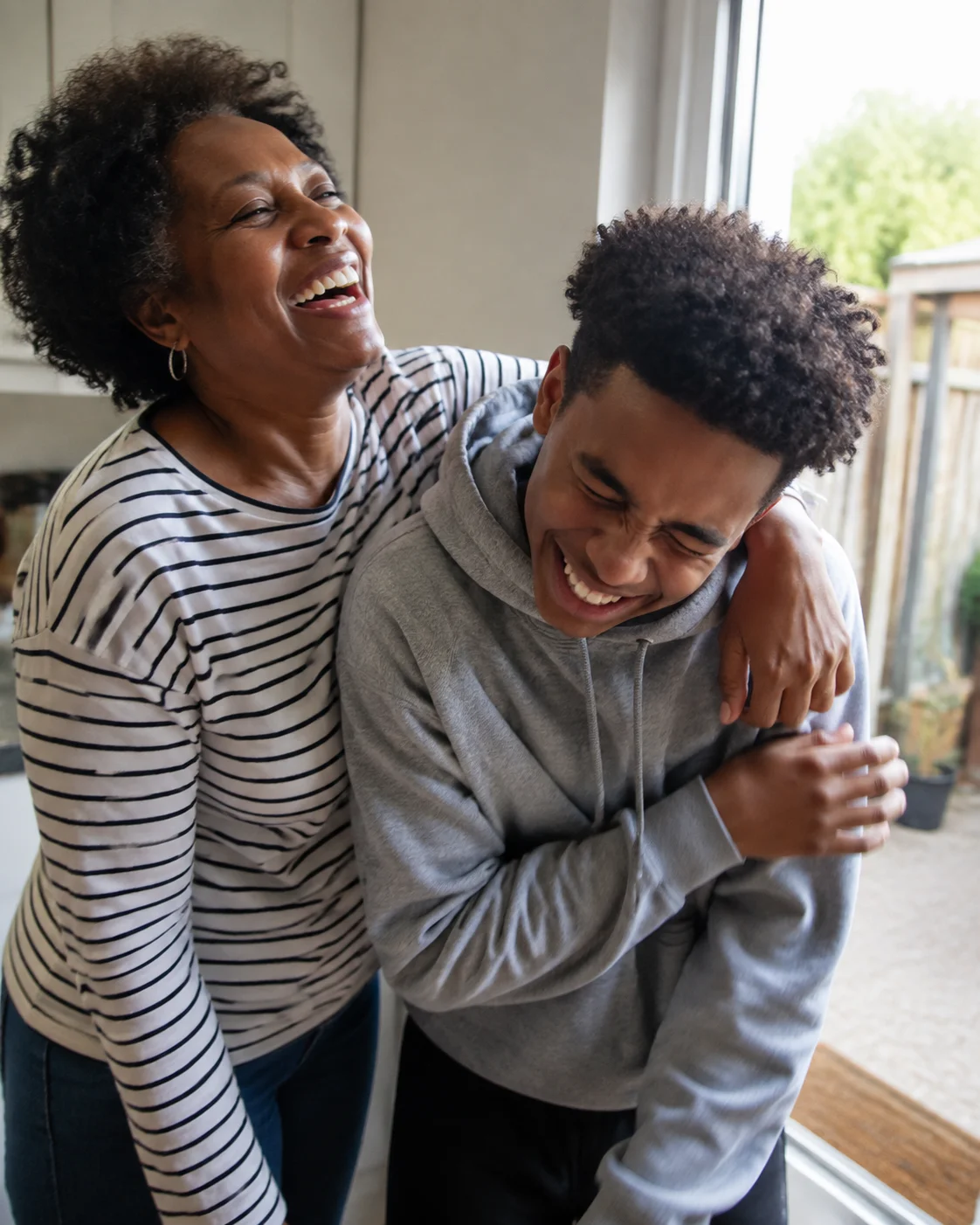 An adult and teenager laughing together in a playful side hug at home