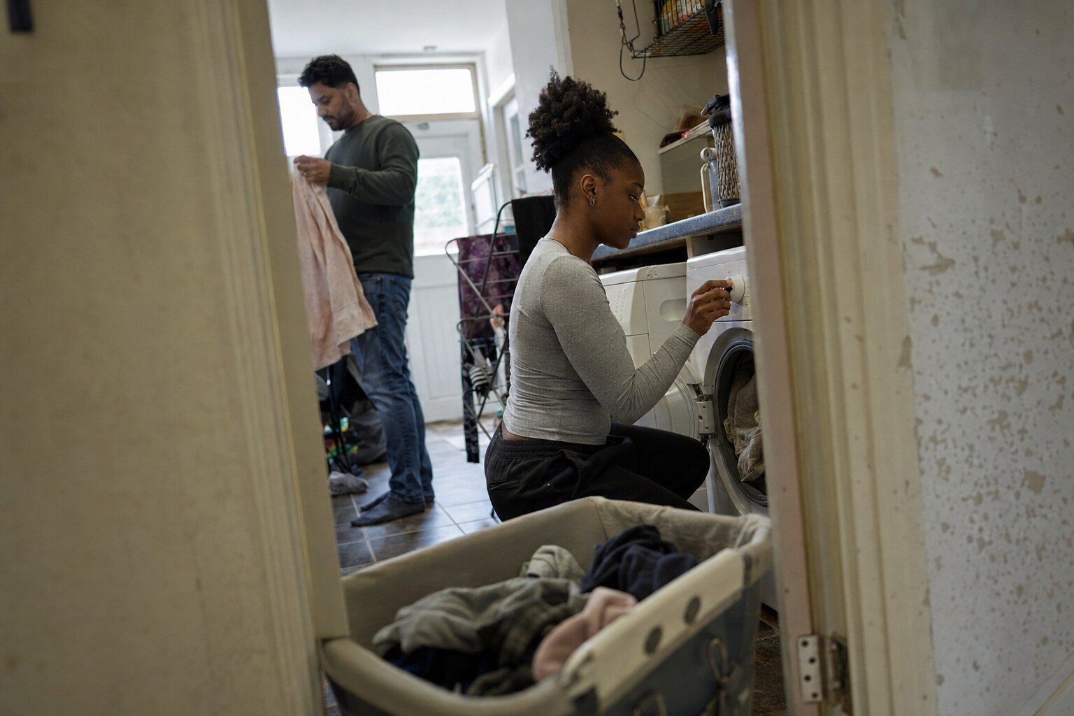 A foster carer showing a teenage girl how to use the washing machine in a London kitchen