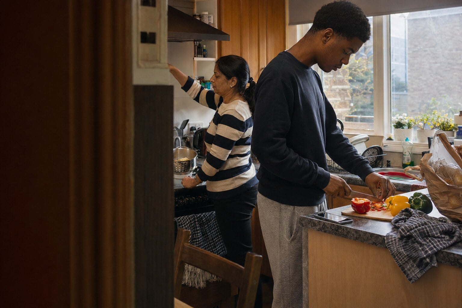 A young adult and their former foster carer sitting together at a kitchen table at home