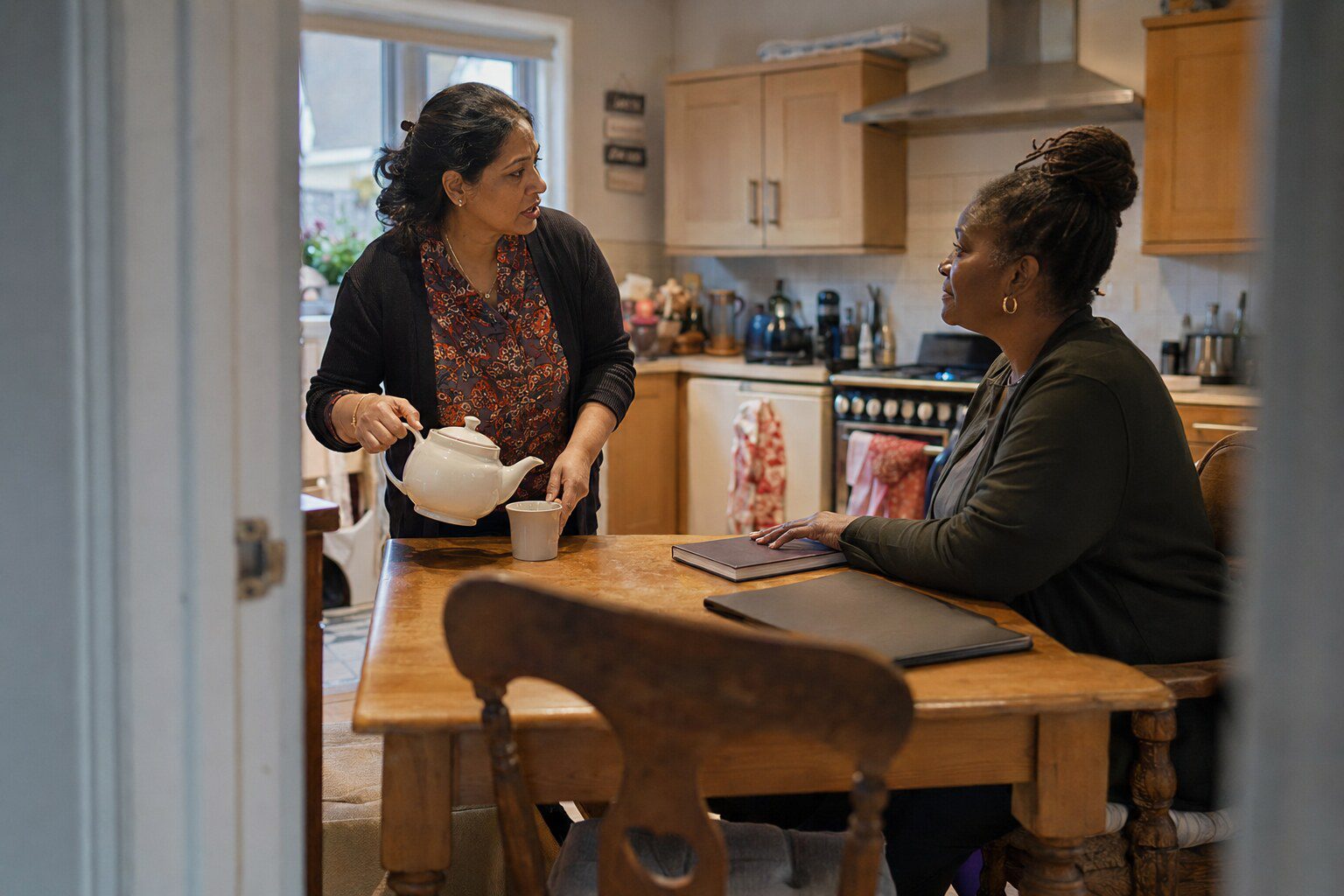 A foster carer sitting at a kitchen table talking with her supervising social worker over a cup of tea